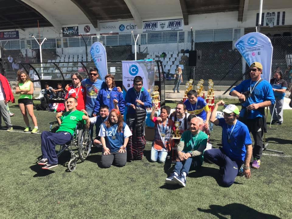 Fotografía de un grupo de personas con discapacidad en una cancha de fútbol. Cada uno de ellos tiene una medalla colgando del cuello, lo que indica que han participado en un evento